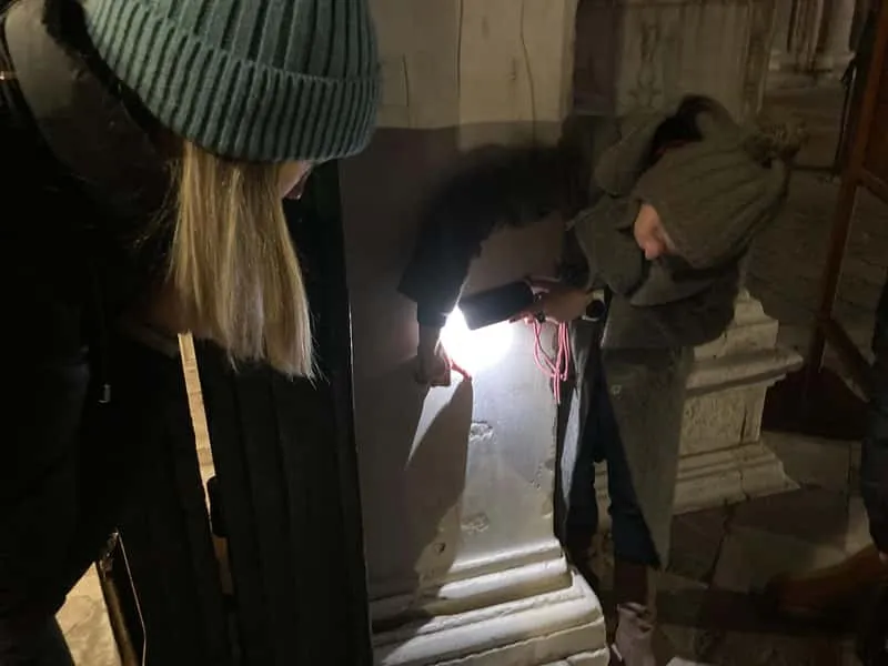 Narrow Venice alleyway lit by lamplight at night with Gothic arches and shadowy doorways on a ghosts and murders evening walking tour in Venice Italy