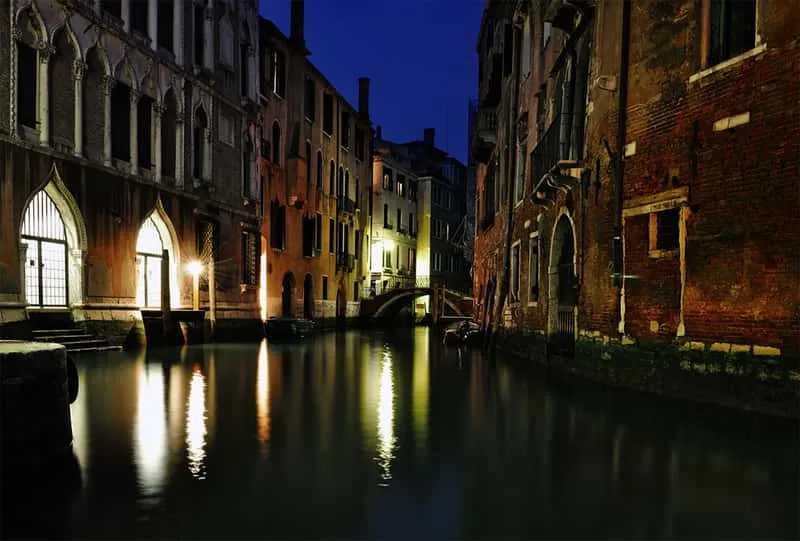 Rialto Bridge lit by warm evening light with reflections in the Grand Canal at dusk on a Venice ghost tour route in Venice Italy
